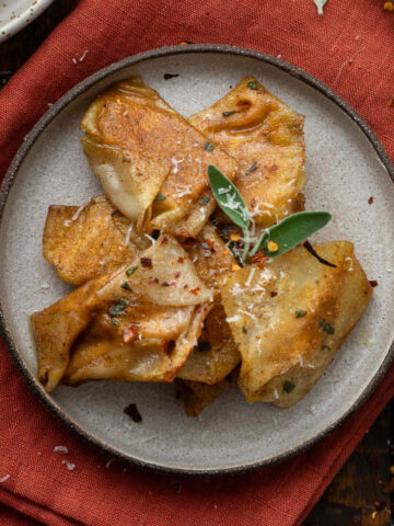 A plate of crispy butternut squash ravioli on a red linen napkin.