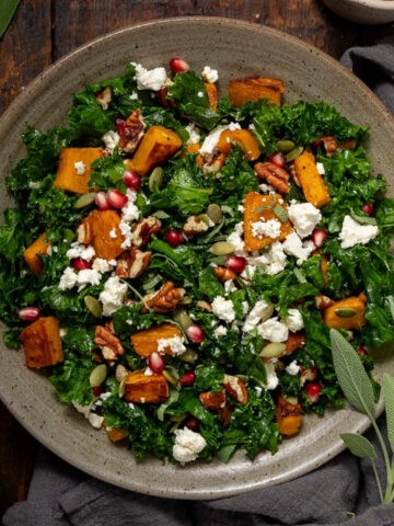 Roast pumpkin salad on a plate next to a fork and a sprig of sage.