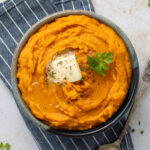 Whipped sweet potatoes garnished with butter, thyme, and parsley in a bowl on top of a blue and white striped napkin.