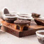 Dark chocolate caramel cups on a cutting board, one in the center with caramel leaking out.