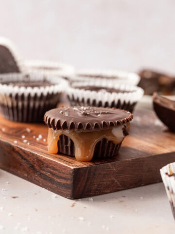 Dark chocolate caramel cups on a cutting board, one in the center with caramel leaking out.