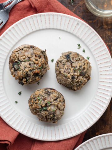 Three vegetarian boursin stuffed mushrooms on a white plate next to a glass of white wine.