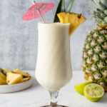 Pina Colada mocktail in a glass garnished with a paper umbrella and pineapple.