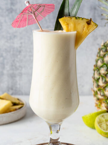 Pina Colada mocktail in a glass garnished with a paper umbrella and pineapple.