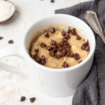 Chocolate chip mug cake next to a gray linen napkin surrounded by mini chocolate chips.