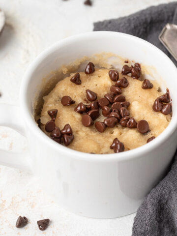 Chocolate chip mug cake next to a gray linen napkin surrounded by mini chocolate chips.