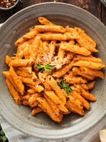 A shallow bowl of penne alla vecchia bettola topped with parmesan cheese and fresh oregano.