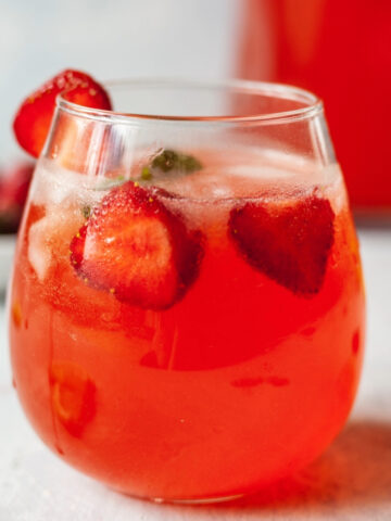 A glass of strawberry lemonade garnished with strawberries and mint.