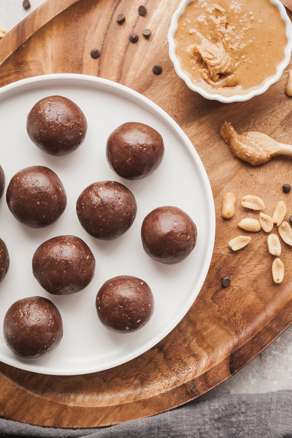 Top down view of a plate of chocolate peanut butter protein balls next to a small bowl of peanut butter.