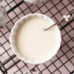 A bowl of vanilla icing with a spoon in it.