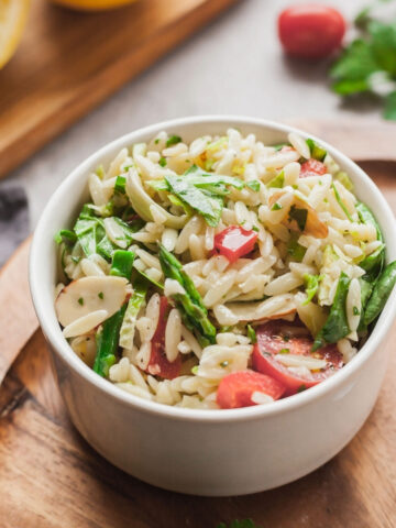 A small bowl of vegan orzo salad on a wood serving platter next to a fork.