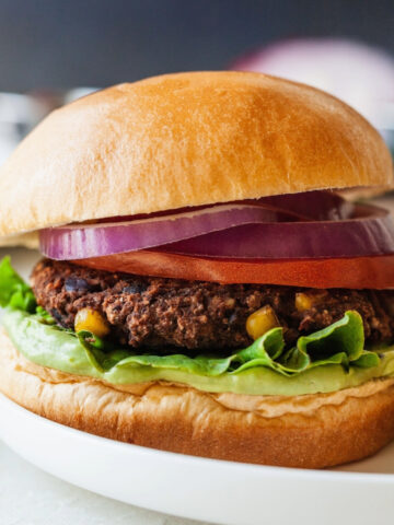 Black bean burger on a plate topped with lettuce, tomato, red onion, and avocado whip.