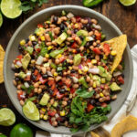 A bowl of Texas caviar with a tortilla chip being dipped into it.