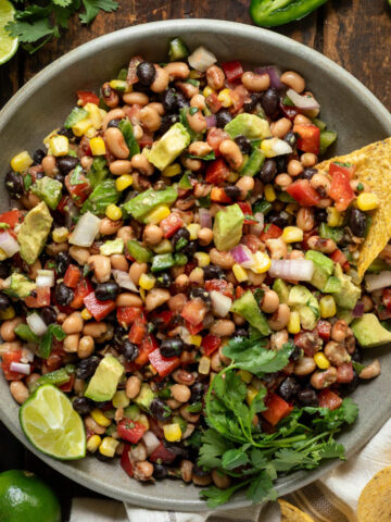 A bowl of Texas caviar with a tortilla chip being dipped into it.