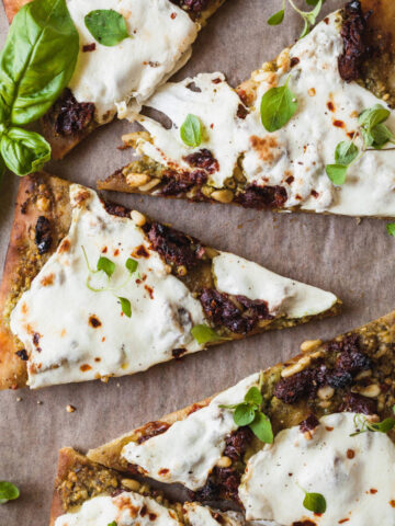 Slices of pesto flatbread pizza on a sheet of parchment paper.