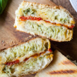 Roasted tomato and pesto panini cut in half on a cutting board.