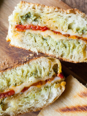 Roasted tomato and pesto panini cut in half on a cutting board.