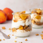 A peach parfait in a little glass jar with a spoon next to it.