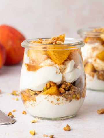 A peach parfait in a little glass jar with a spoon next to it.