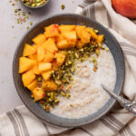 A bowl of breakfast quinoa topped with peaches and pistachios.
