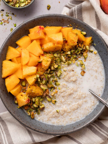 A bowl of breakfast quinoa topped with peaches and pistachios.