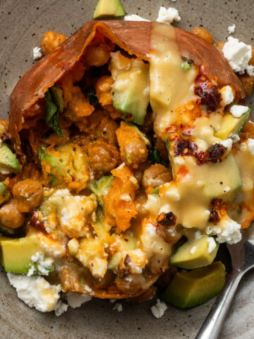 A sweet potato stuffed with crispy chickpeas, spinach, feta, avocado, and chili crisp with a fork next to it.