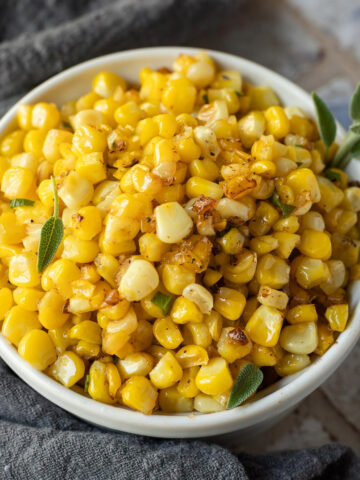 A bowl of buttered sweet corn next to a gray linen napkin.