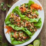 Vegan lettuce wraps on a white platter with limes and a small bowl of peanuts in the background.