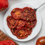 Slices of oven dried tomatoes on a white plate with a fork in it.