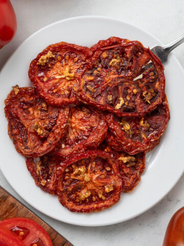 Slices of oven dried tomatoes on a white plate with a fork in it.