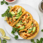 Three breakfast tacos on a white platter next to a small bowl of salsa and lime wedges.