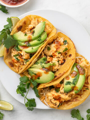 Three breakfast tacos on a white platter next to a small bowl of salsa and lime wedges.