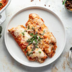 Two spinach and cheese manicotti on a white plate topped with basil.