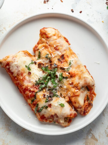 Two spinach and cheese manicotti on a white plate topped with basil.