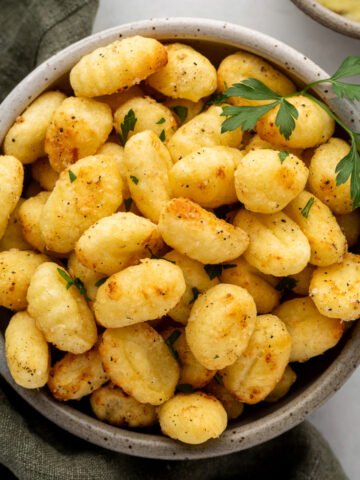 Air fryer gnocchi in a bowl garnished with a sprig of parsley.