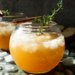 Apple cider mocktail in a round glass garnished with thyme and a cinnamon stick.