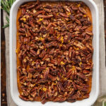 Savory sweet potato casserole on a striped linen napkin surrounded by fresh herbs.