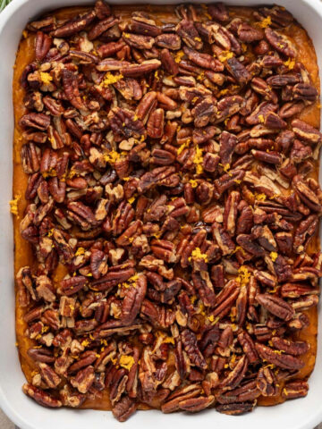 Savory sweet potato casserole on a striped linen napkin surrounded by fresh herbs.