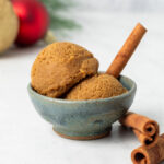 Two scoops of edible gingerbread cookie dough in a small bowl with cinnamon sticks around as decor.