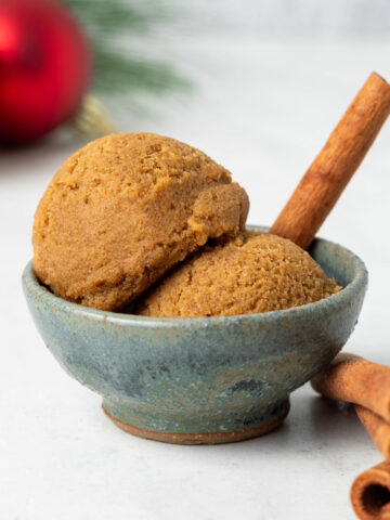 Two scoops of edible gingerbread cookie dough in a small bowl with cinnamon sticks around as decor.