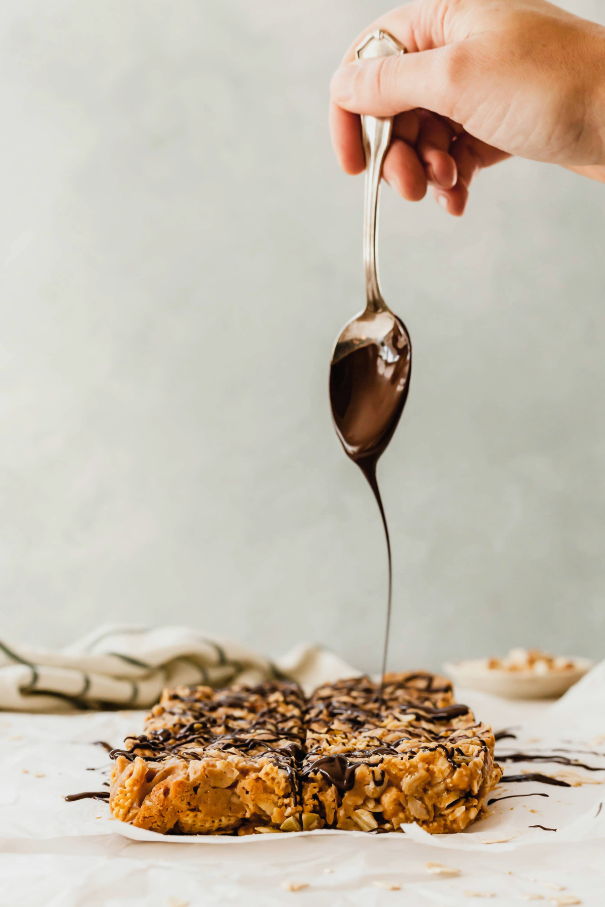 A hand holding a spoon drizzling chocolate over a batch of peanut butter breakfast bars.