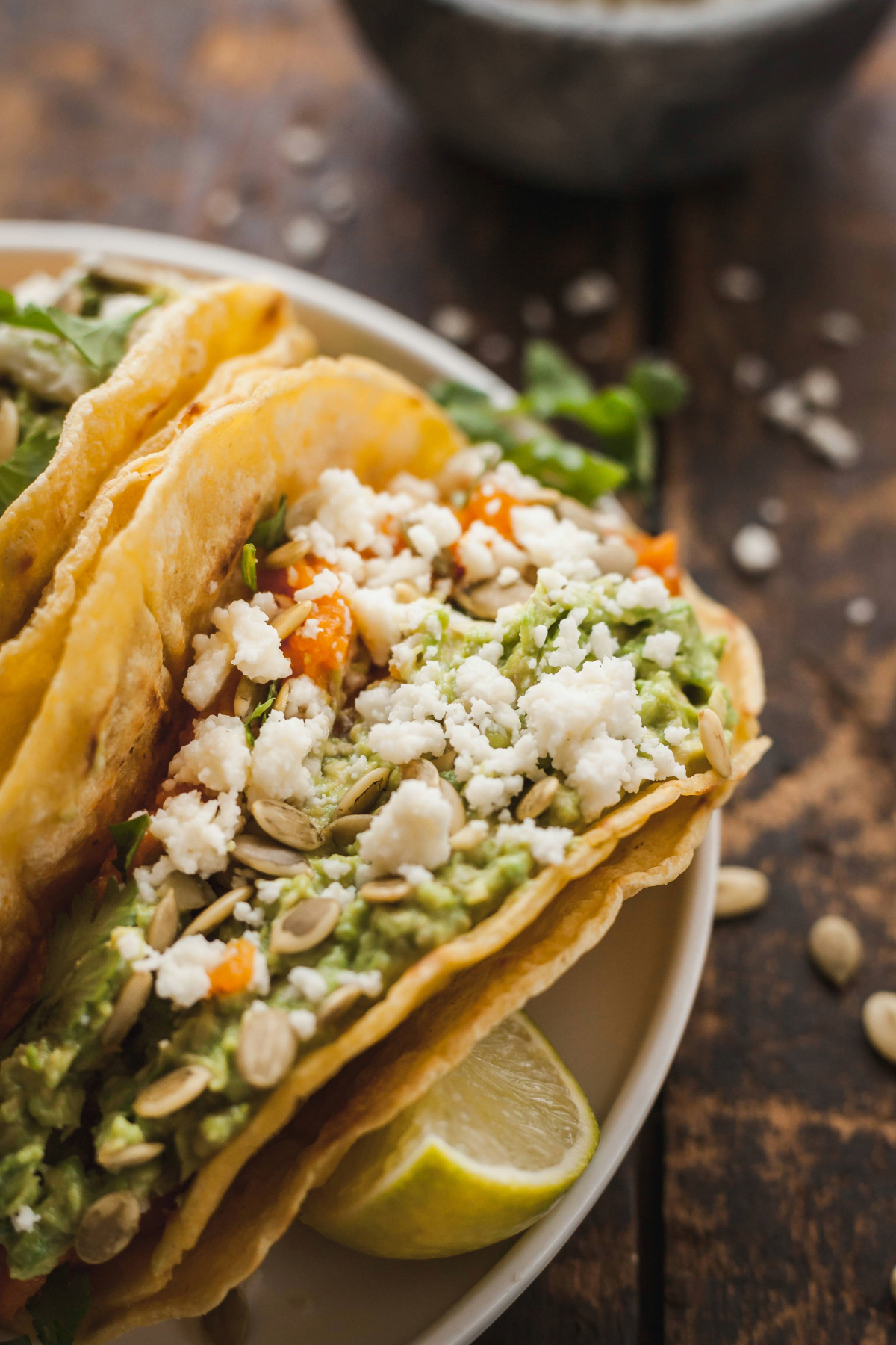 A close up on a mashed sweet potato taco next to a lime wedge and a bowl of queso fresco.