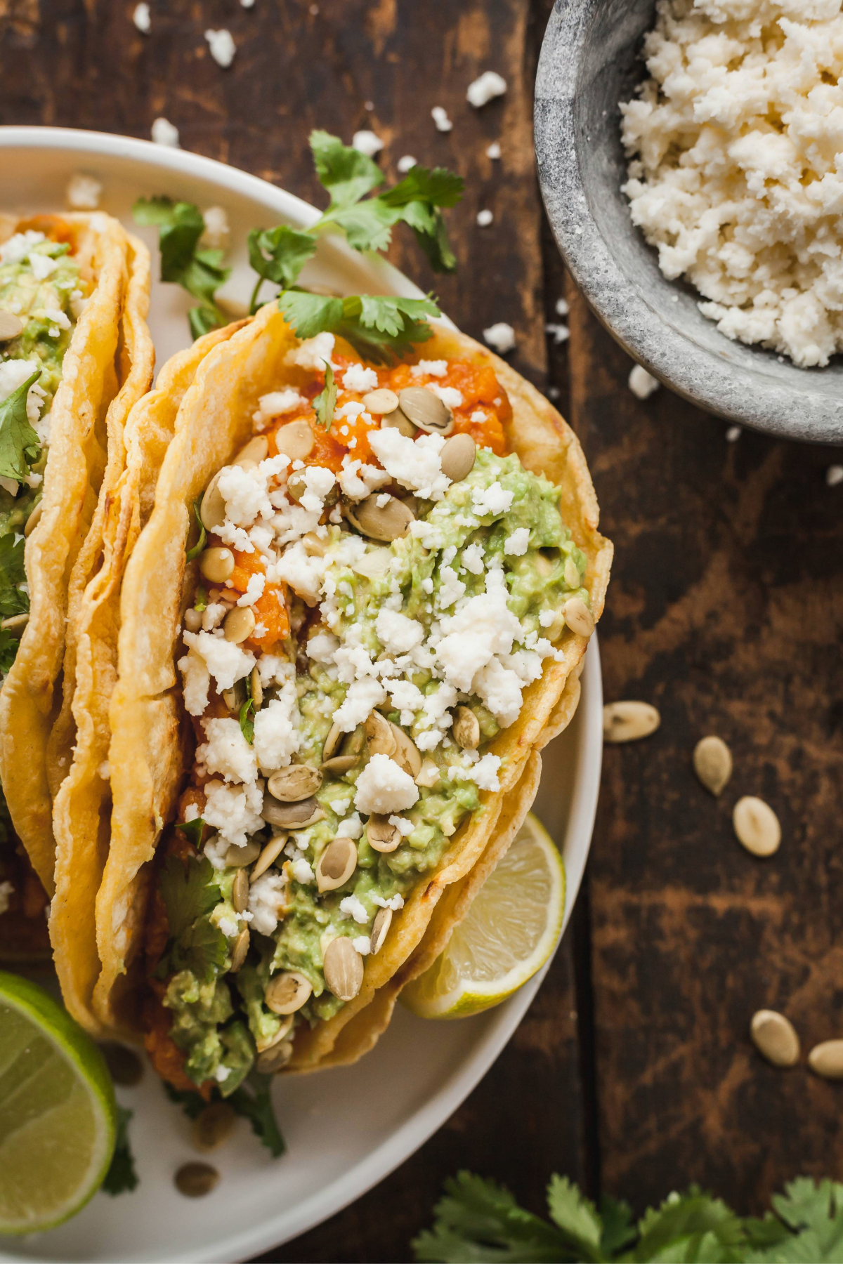 A close up on a mashed sweet potato taco next to a lime wedge and a bowl of queso fresco.