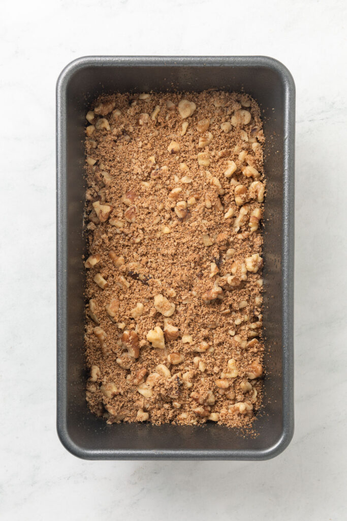 Cinnamon swirl banana bread batter topped with cinnamon and walnuts in a loaf pan.