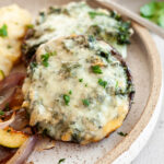 Two spinach stuffed portobello mushrooms on a plate next to a serving of mashed potatoes.