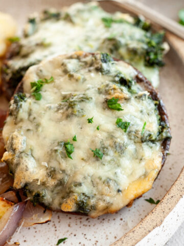 Two spinach stuffed portobello mushrooms on a plate next to a serving of mashed potatoes.