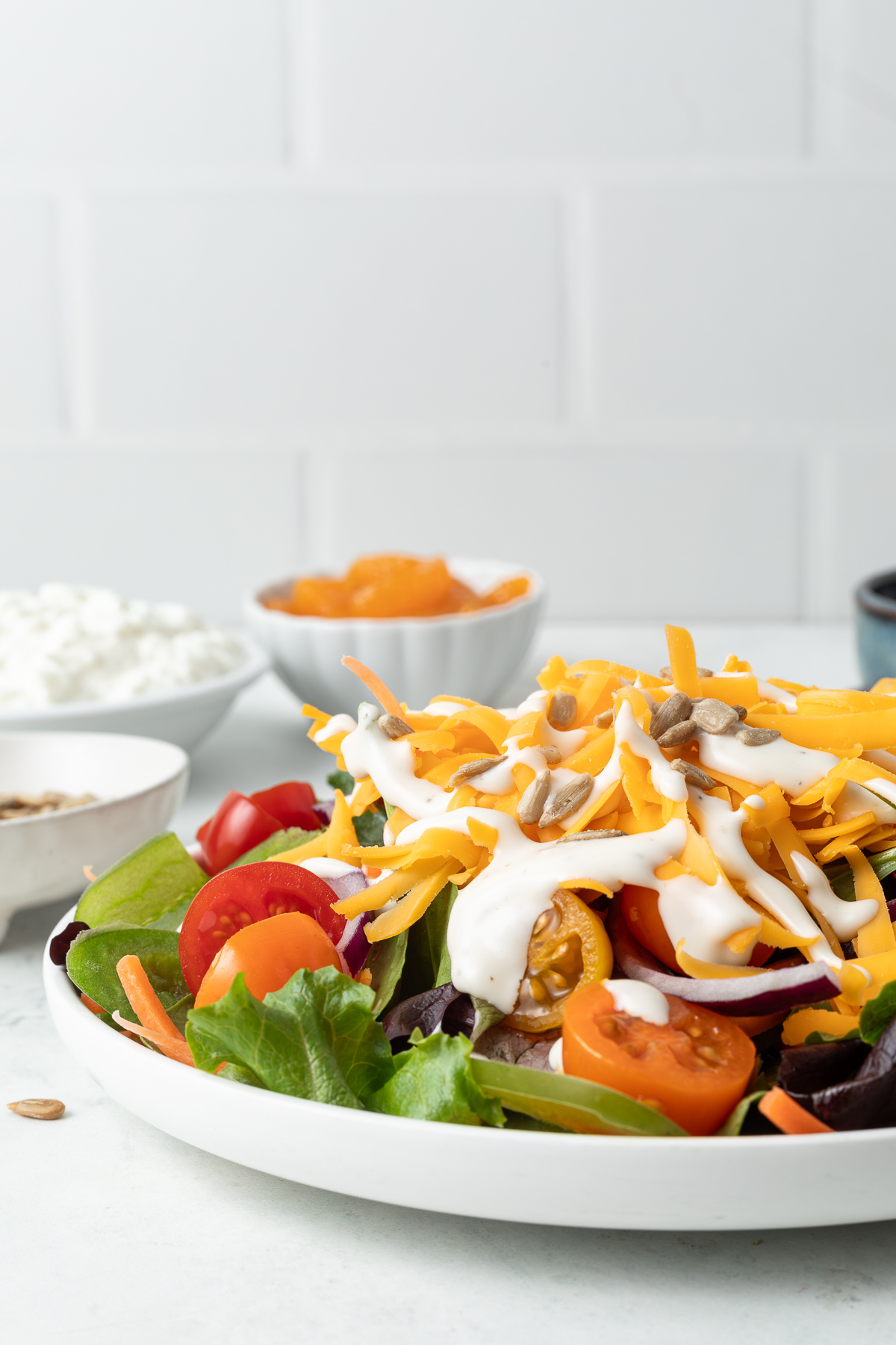 Side view of a salad in a white plate next to a gray linen napkin. In the background you can see the ingredients that went into the salad portioned into small bowls.
