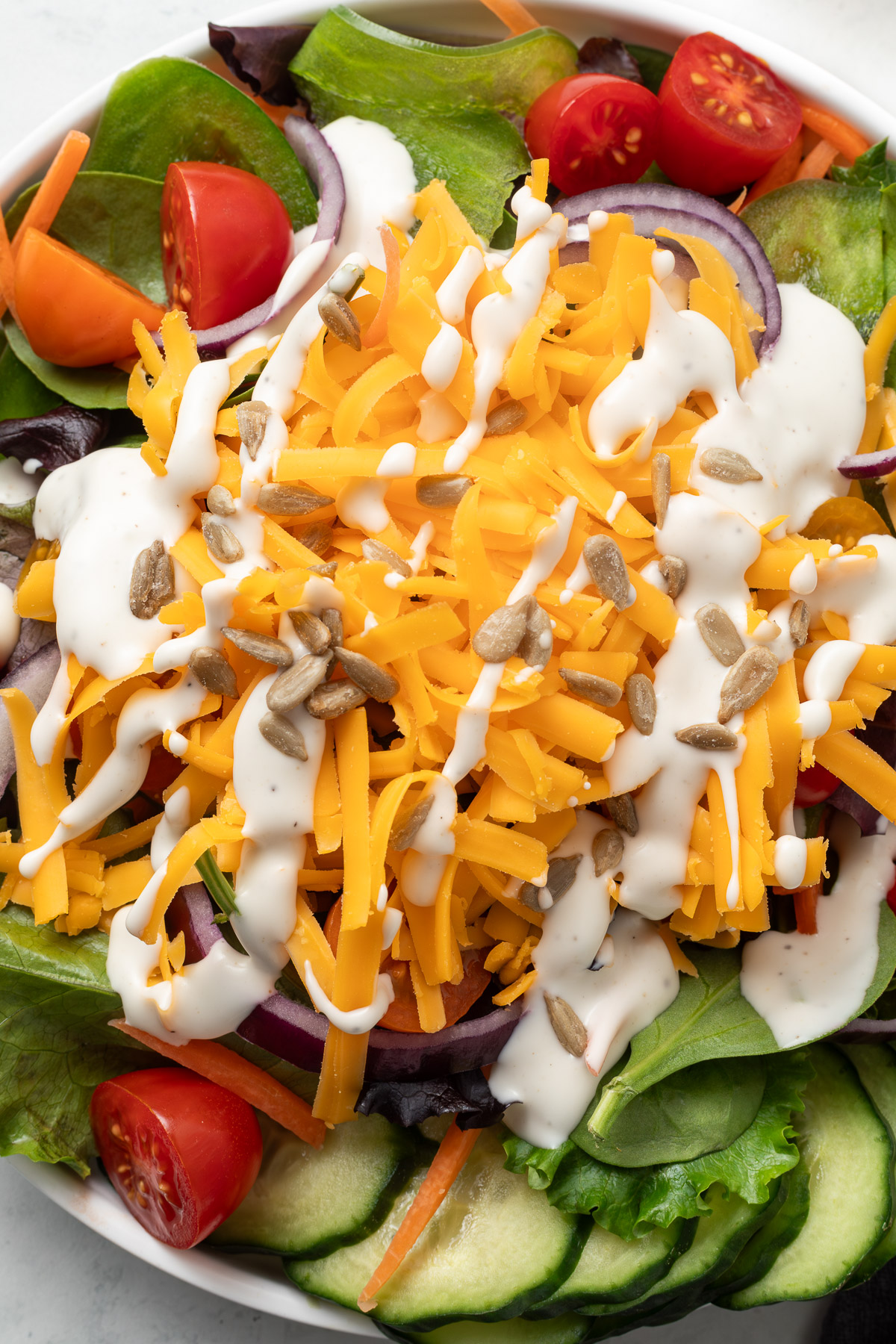 Close up of a Salad Bar Salad topped with cheddar cheese and a drizzle of ranch dressing.