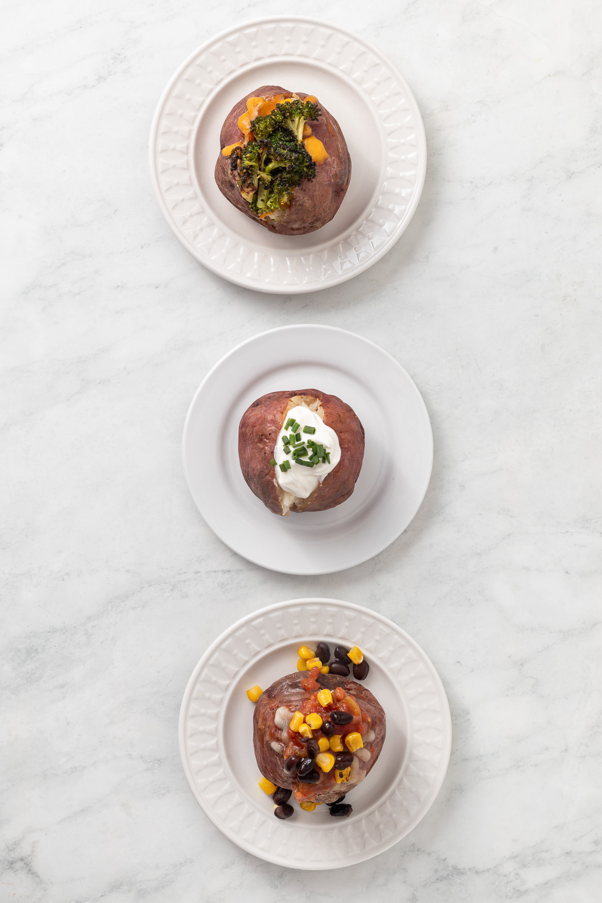 Three baked potatoes on individual plates topped with different toppings.