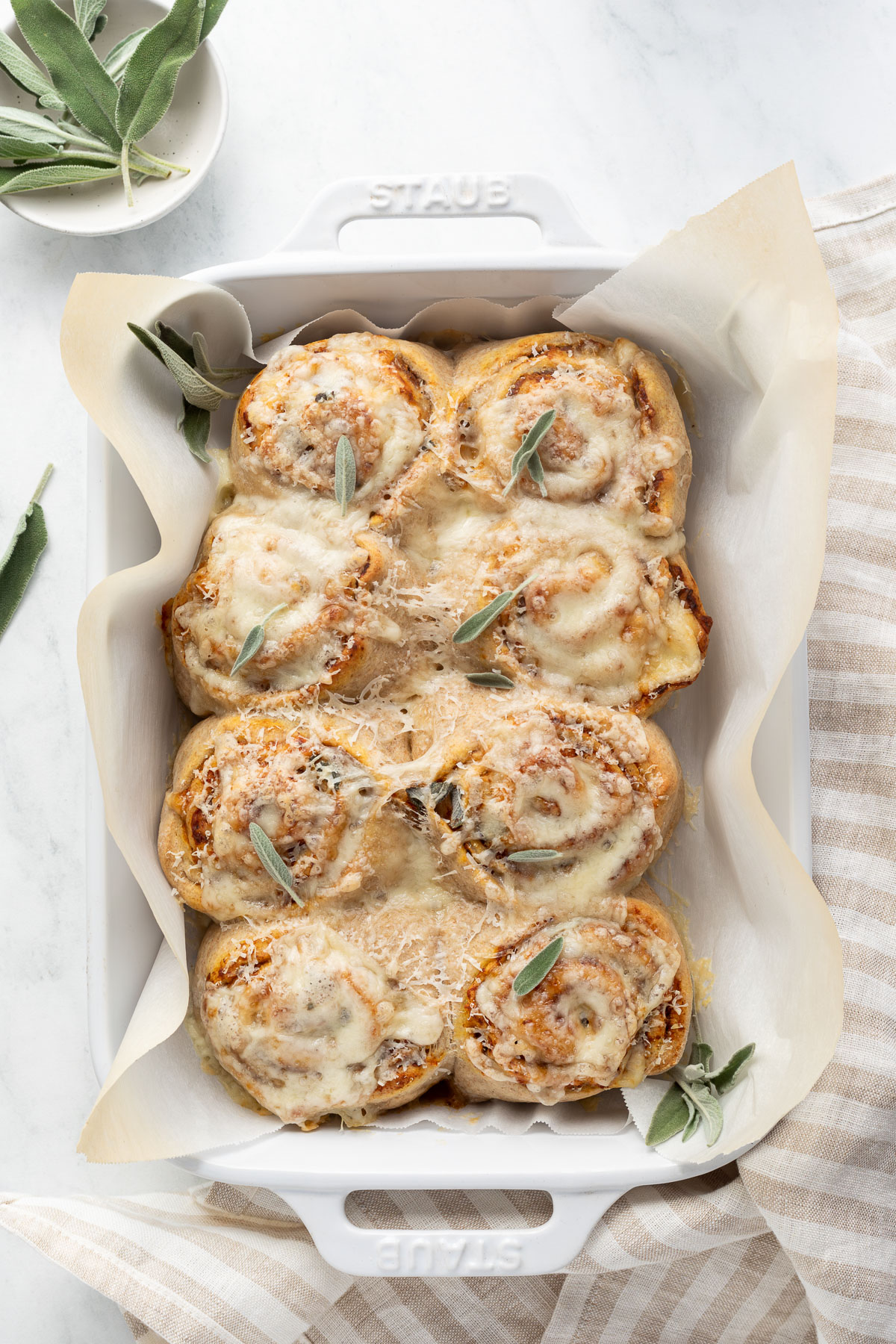 Butternut squash rolls in a baking dish topped with fresh sage.